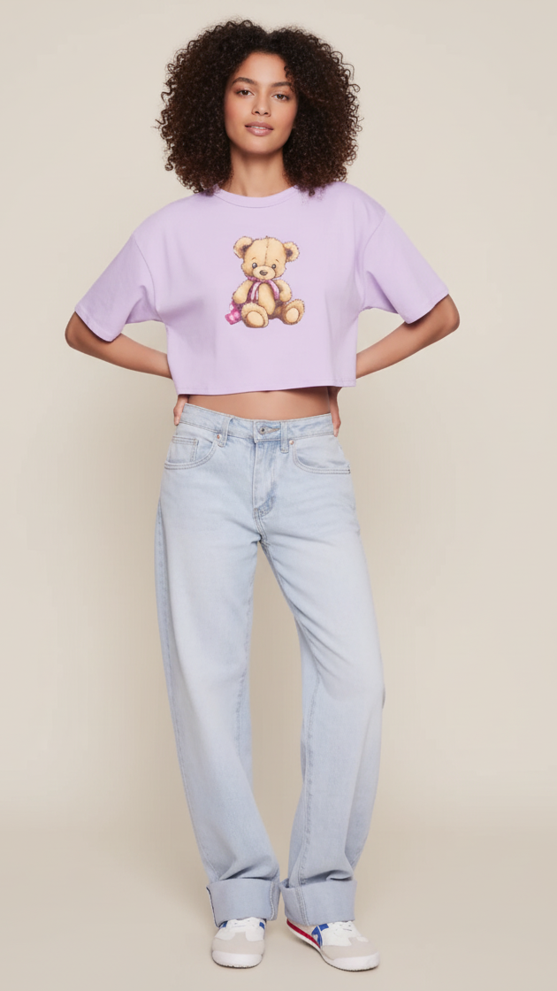Person wearing a purple t-shirt with a teddy bear graphic and light blue jeans on a beige background