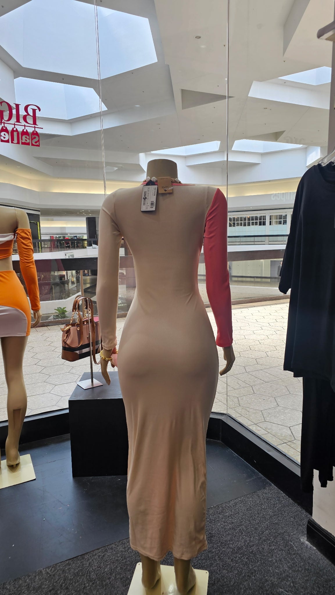 Mannequin wearing a beige dress with a visible tag in a store setting.